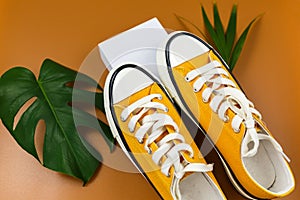 Orange sneakers on white geometry shapes with tropic leaves on brown background. Trendy fashion accessories. Flat lay, close up.