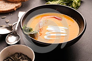 Orange soup with shrimp, sour in dark bowlon and bread near silver spoons