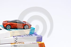 An orange sports car toy placed over bundles of money notes showing wealth and saving concept
