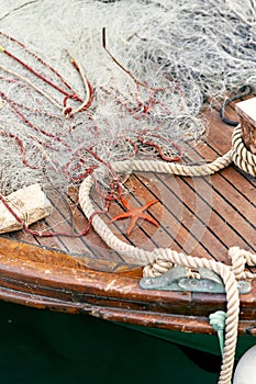 Orange starfish lies on a wooden deck of a boat near a rope and a fishing net. Close up