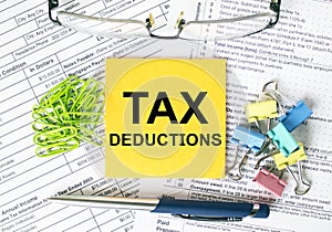 Orange sticker with text Tax Deductions. Colored stationery clips, green paper clips and eyeglasses