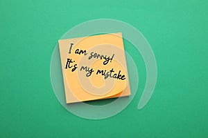 Orange sticky note with phrase I Am Sorry, It\'s My Mistake on green background, top view