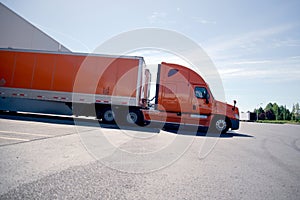 Orange stylish semi truck trailer unloading cargo in warehouse