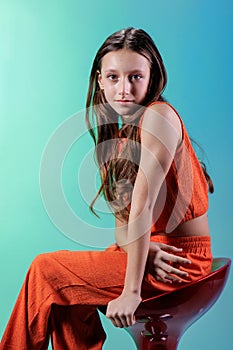 In an orange suit, a beautiful girl model poses while sitting on a red chair