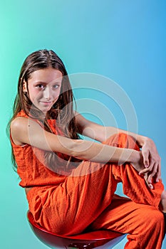In an orange suit, a beautiful girl model sitting posing on a light blue background