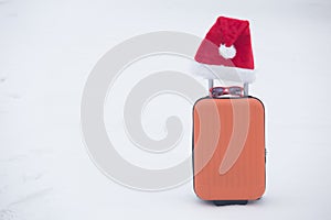 Orange suitcase with sunglasses and santa hat on snow. Copy space