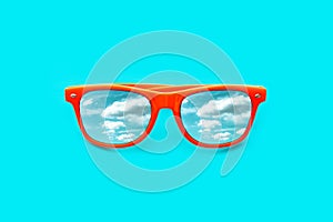 Orange sunglasses with blue sky with clouds reflections isolated in intense cyan blue background.