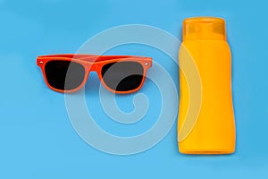 Orange sunglasses and orange bottle of suncream or sun lotion isolated flat lay in an intense blue background.