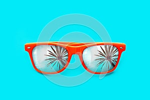 Orange sunglasses with palm tree reflections isolated in intense cyan blue background. Minimal image concept for ready for summer