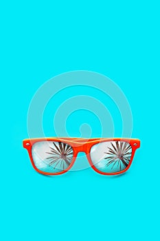 Orange sunglasses with palm tree reflections isolated in intense cyan blue background. Minimal image concept for ready for summer