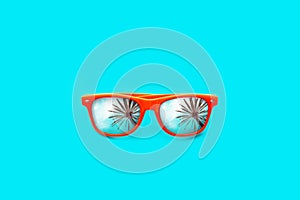 Orange sunglasses with palm tree reflections in large empty intense cyan blue background. Minimal image.