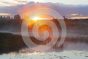 Orange sunny light with rays and shadows over the foggy river at dawn