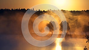 Orange sunrise on the lake or the river, morning mist at sunrise. Orange rays of the sun through the morning mist on the