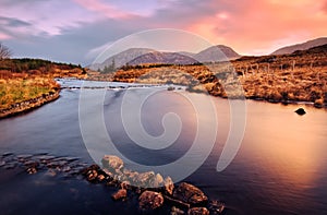 Orange sunrise landscape scenery with river and mountains under dramatic skies at Derryclare, connemara, galway, Ireland