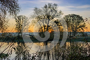 Orange sunrise over river surface against blue sky. River landscape in autumn morning