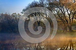 Orange sunrise over the river surface with fog in autumn morning. River landscape at sunrise