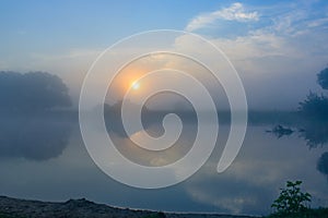 Orange sunrise over the river surface with fog in summer morning. River landscape at sunrise