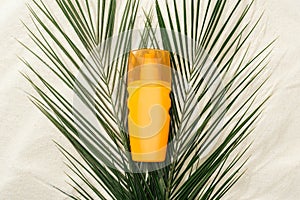 Orange sunscreen lotion on green palm leaves on sand.