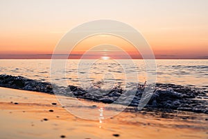 Orange sunset at a beach of the baltic sea on the German island Rugia with breaking wave in the foreground