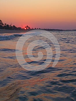 Orange sunset on the beach inside the sea with waves