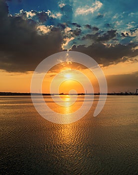 Orange sunset in dramatic clouds over water