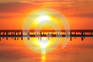 Orange sunset, dramatic and majestic sky over beach with sun reflection in water. Wood posts for salt extraction of