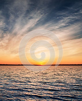 Orange sunset in low dramatic clouds over water