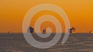 Orange sunset in ocean. Rays of setting sun illuminate hulls of ships on horizon