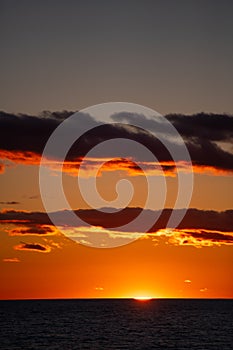 Orange sunset over lake Ontario at dusk in the evening sun setting below the horizon