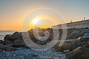 Orange sunset on the seashore with large stones