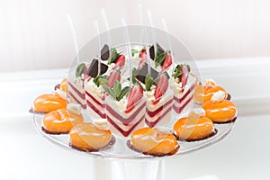 Orange sweets and creamy berry desserts in cups with fresh strawberries and mint