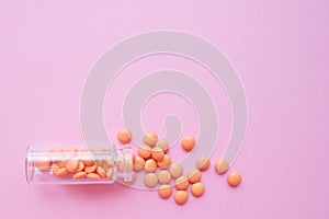 Orange tablets from glass bottle on pink background. copyspace for text. Epidemic, painkillers, healthcare, treatment pills and