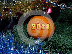 Orange tangerine on the Christmas tree with the numbers of the new year 2023. A greeting card for the new year 2023.