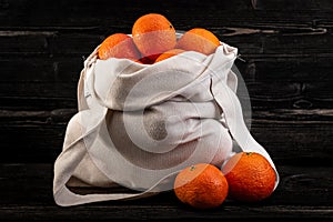 Orange tangerine friuts fall out or tip out from white shopper bag on rustic wooden table