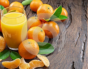 Orange tangerine fruits and glass of fresh tangerine juice on dark wooden background