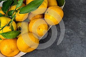 orange tangerines with green leaves in a cardboard tray on a table