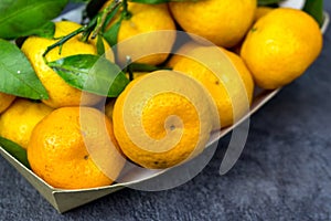 orange tangerines with green leaves in a cardboard tray on a table