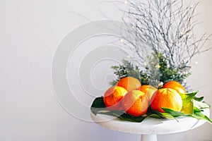Orange tangerines on grey background in New Year`s decor with brown pine cones and green leaves. Christmas decoration with