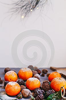 Orange tangerines on grey background in New Year`s decor with brown pine cones and green leaves. Christmas decoration with