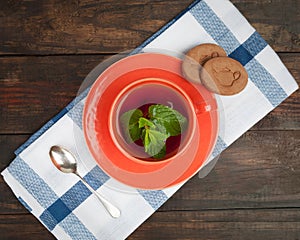 Orange tea cup with spoon and cookies, top view.