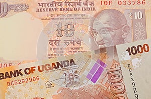 A orange ten rupee bill from India paired with a orange and white one thousand shilling bill from Uganda.