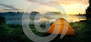 Orange tent on the bank of the river covered with fog in early morning