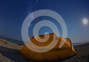 Orange tent on the beach at night under the starry sky