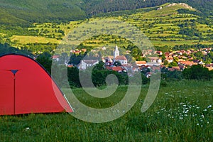 Orange tent on a green hill with sunrise views towards Rimetea village, Alba county, Romania - early morning, Summer. Copy space.