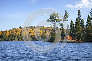 Orange tent on rocky shore of an island on a northern Minnesota trout lake during autumn
