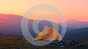 An orange tent stands against the background of a mountain range in the warm sunset light. Hiking in the mountains