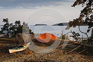 Orange tent, yellow kayak on the island. Sunset, evening time. Kayaking, camping equipment, outdoor activities