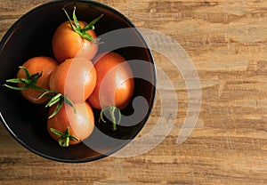 Orange tomatoes in a white bowl on wood background