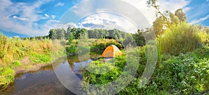 Orange tourist tent on bank of river with banks