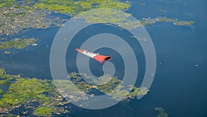 An orange traffic cone floating in a eutrophic river water after being thrown in photo